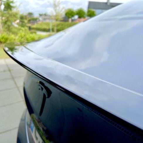 Blank sort ABS-spoiler monteret på bagklappen af en sort Tesla Model 3, set bagfra udendørs