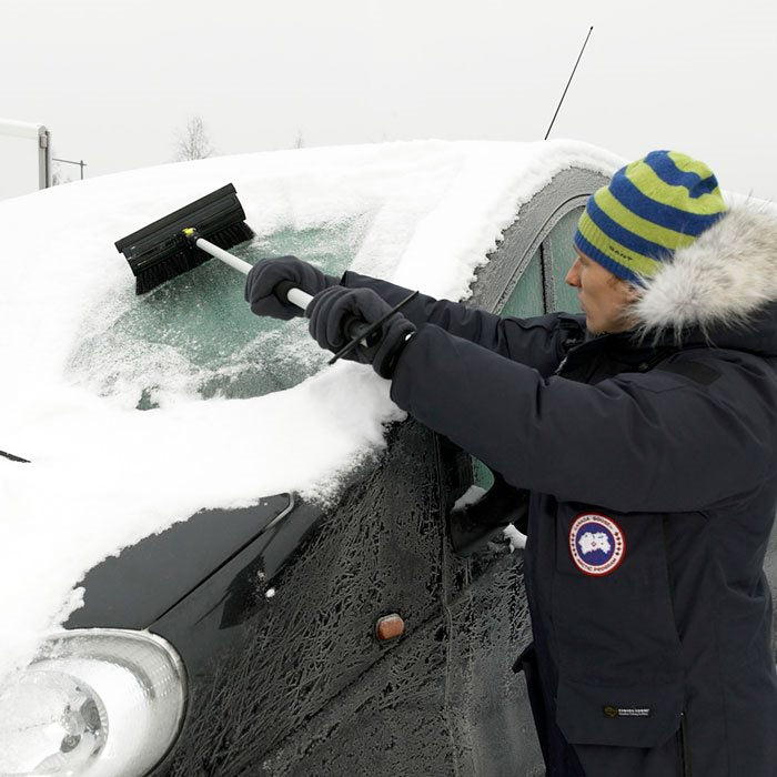 Man som skrapar snö från bilens framruta