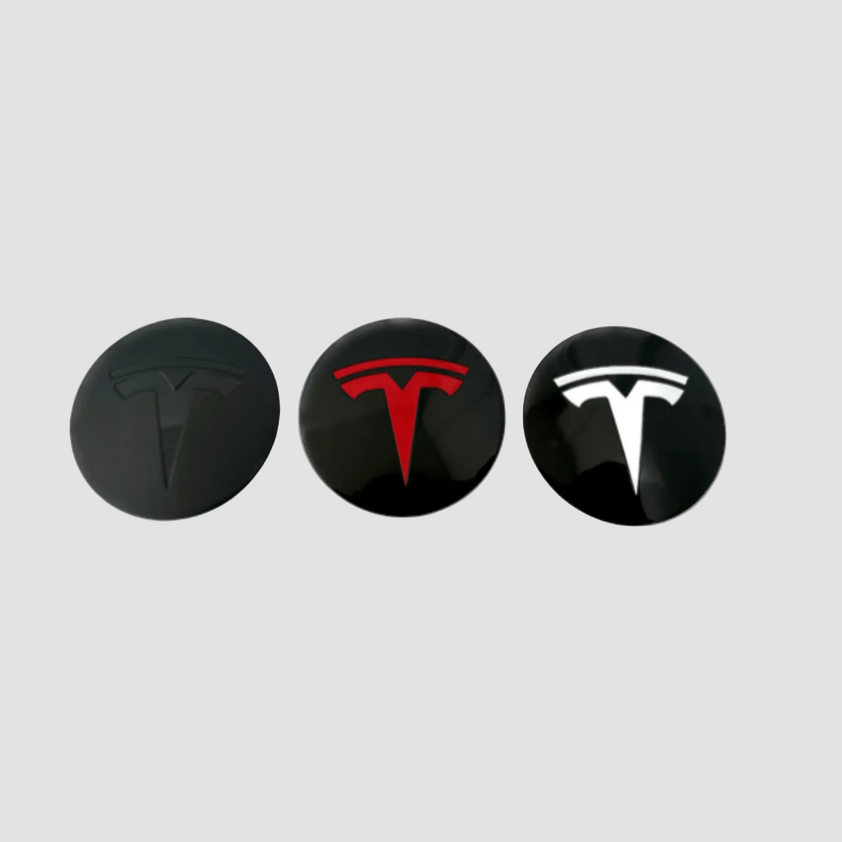 Tre Tesla navkapslar i svart, rött och vitt för fälgar.