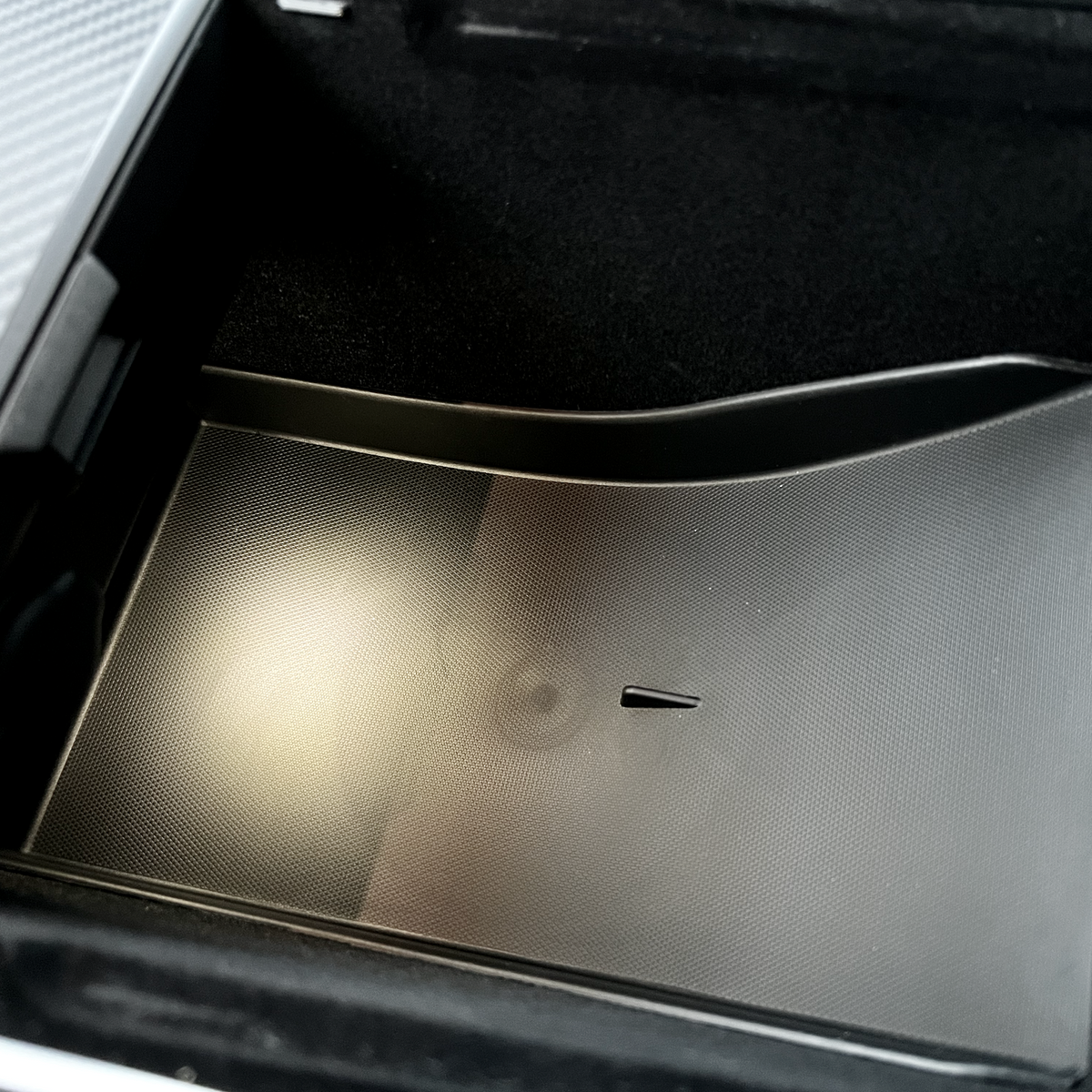 Sort tekstureret underlag/bakke placeret i opbevaringsrummet under armlænet i Tesla Model Y