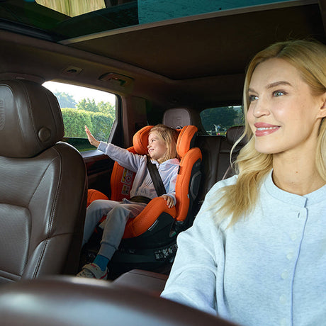 Kvinde kører bil mens barn i Recaro Xenon 1 Kid autostol vinker ud af vinduet