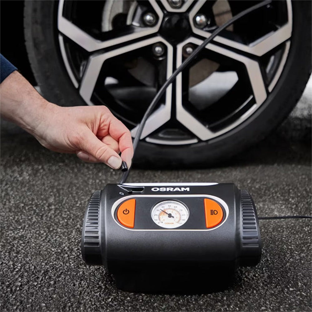Person tilslutter Osram TYREinflate 2110 til bildæk, kompressor placeret på asfalt