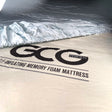 GCG MAX bambuslakan lagt över en madrass, med GCG MAX-logotyp.
