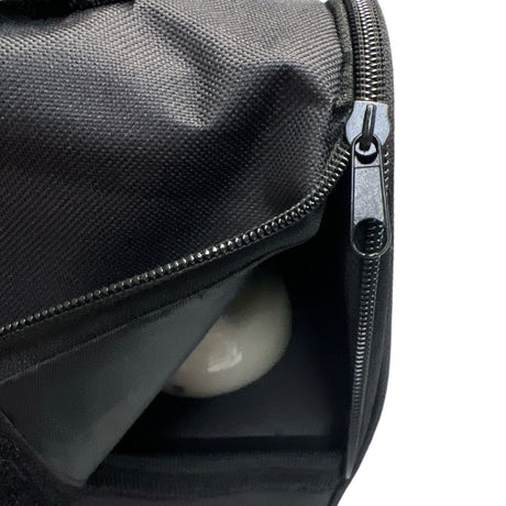 Svart väska med öppen dragkedja och en reflekterande kula inuti