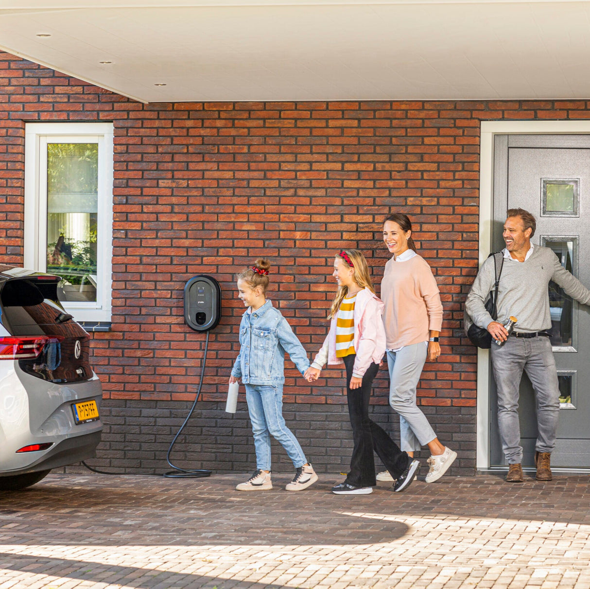 Familj lämnar hus med elbil ansluten till Ratio smart laddbox