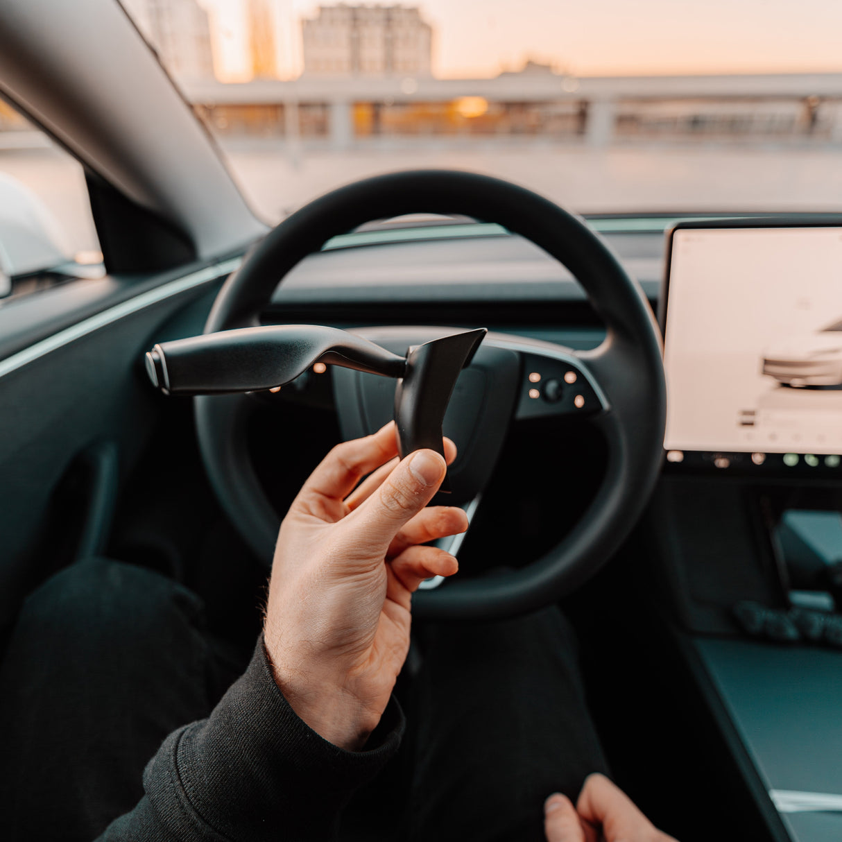 Hand håller S3XY Stalks blinkersarm framför Tesla Model 3 Highland ratt.