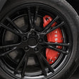 Röda bromsoksskydd med vitt Tesla-logotyp på en svart fälg.