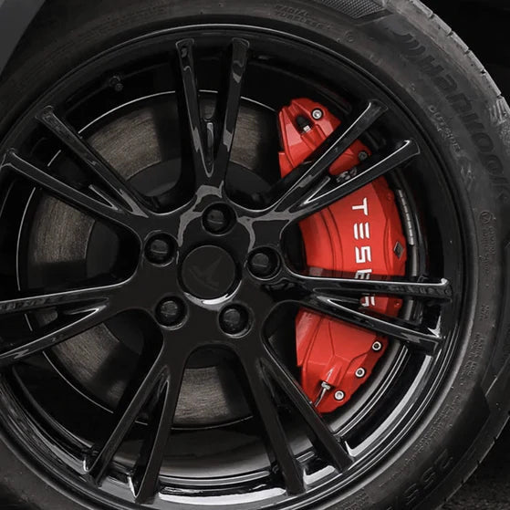 Röda bromsoksskydd med vitt Tesla-logotyp på en svart fälg.
