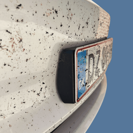 Smutsig vit bil med insektsrester och registreringsskylt