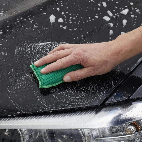 Handtvättar bil med grön svamp och tvålbubblor.