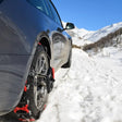 Snökedjor monterade på ett grått bildäck i snötäckta berg