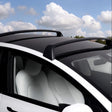 Tesla Model Y med svarta takräcken under en blå himmel med moln